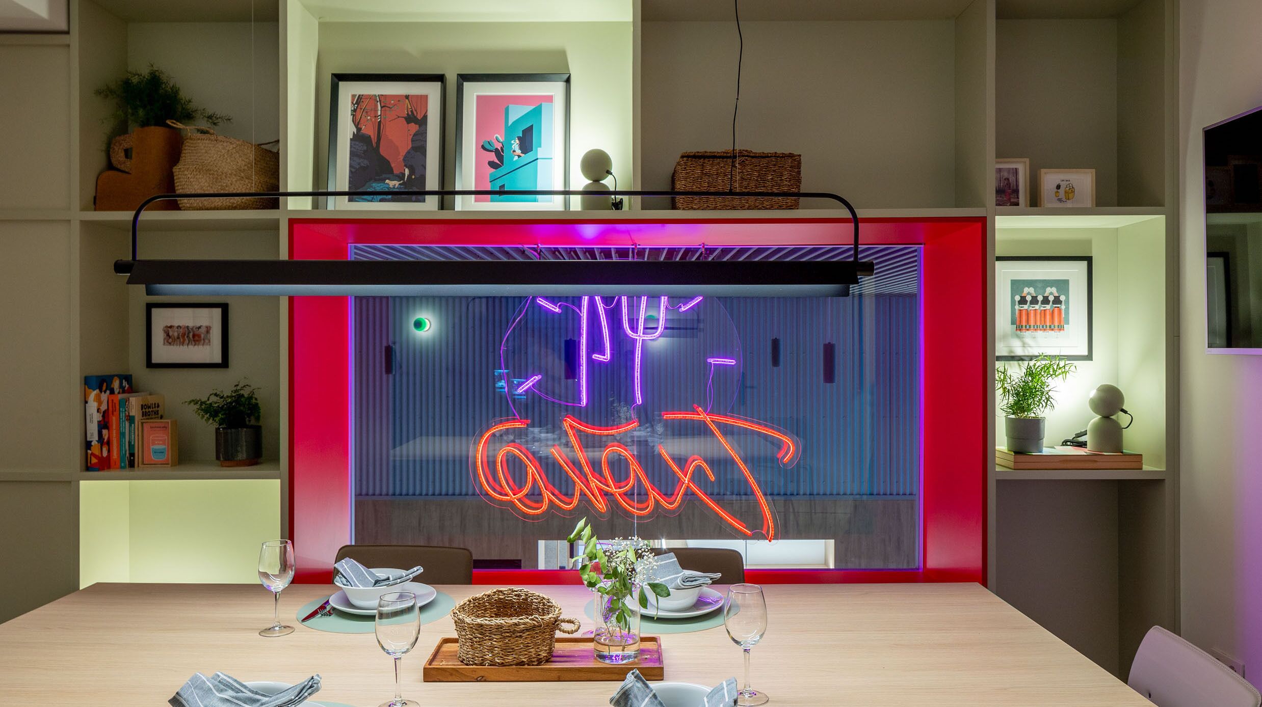 Et moderne spiseområde med en neonlys-skilt, et spisebord dækket med tallerkener, glas og en vase med blomster.