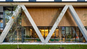 A modern building with a unique triangular architectural design, large glass windows, and a well-maintained garden area. - Aparthotel Kora Green City  (Vitoria-Gasteiz)