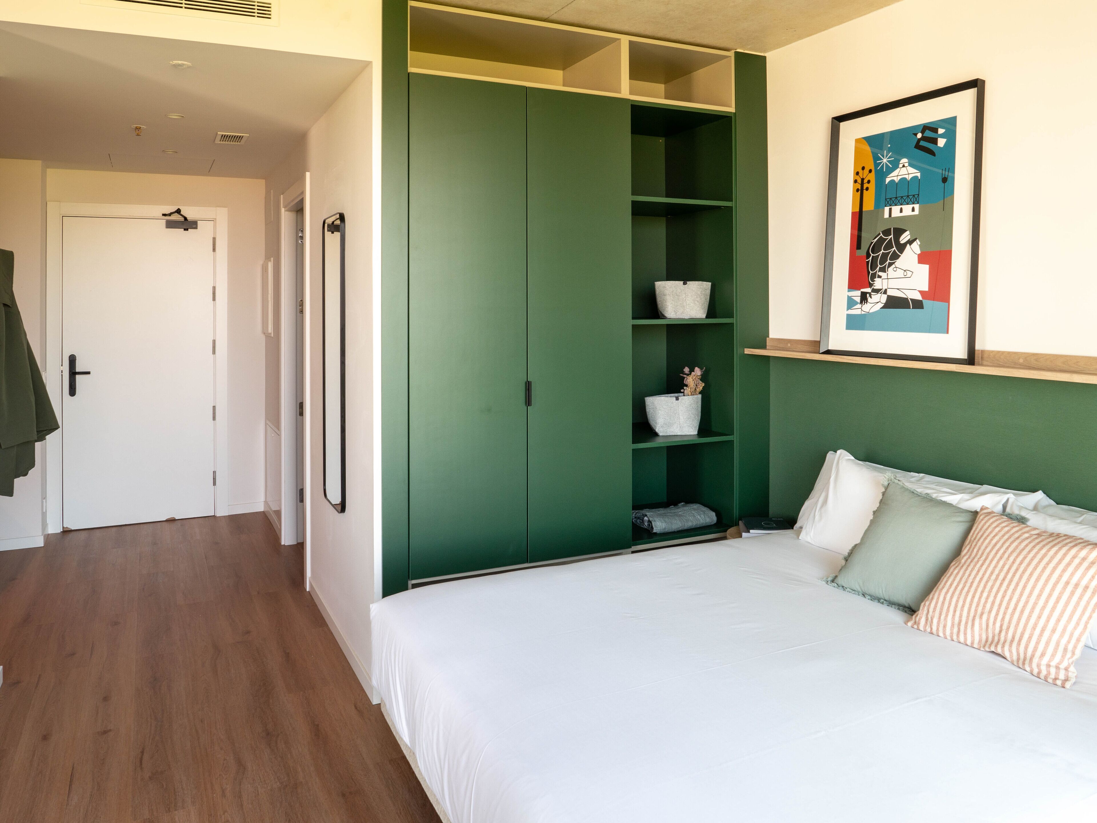 A bedroom with a green wardrobe, a bed with white bedding, and a framed picture on the wall.