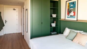A bedroom with a green wardrobe, a bed with white bedding, and a framed picture on the wall.