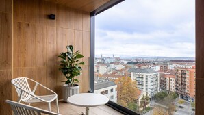 A balcony with two white chairs and a small table, overlooking a cityscape with buildings and trees. - Aparthotel Kora Green City  (Vitoria-Gasteiz)