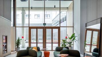 Un vestíbulo moderno con ventanas amplias, sofás verdes, una mesita y plantas en macetas.