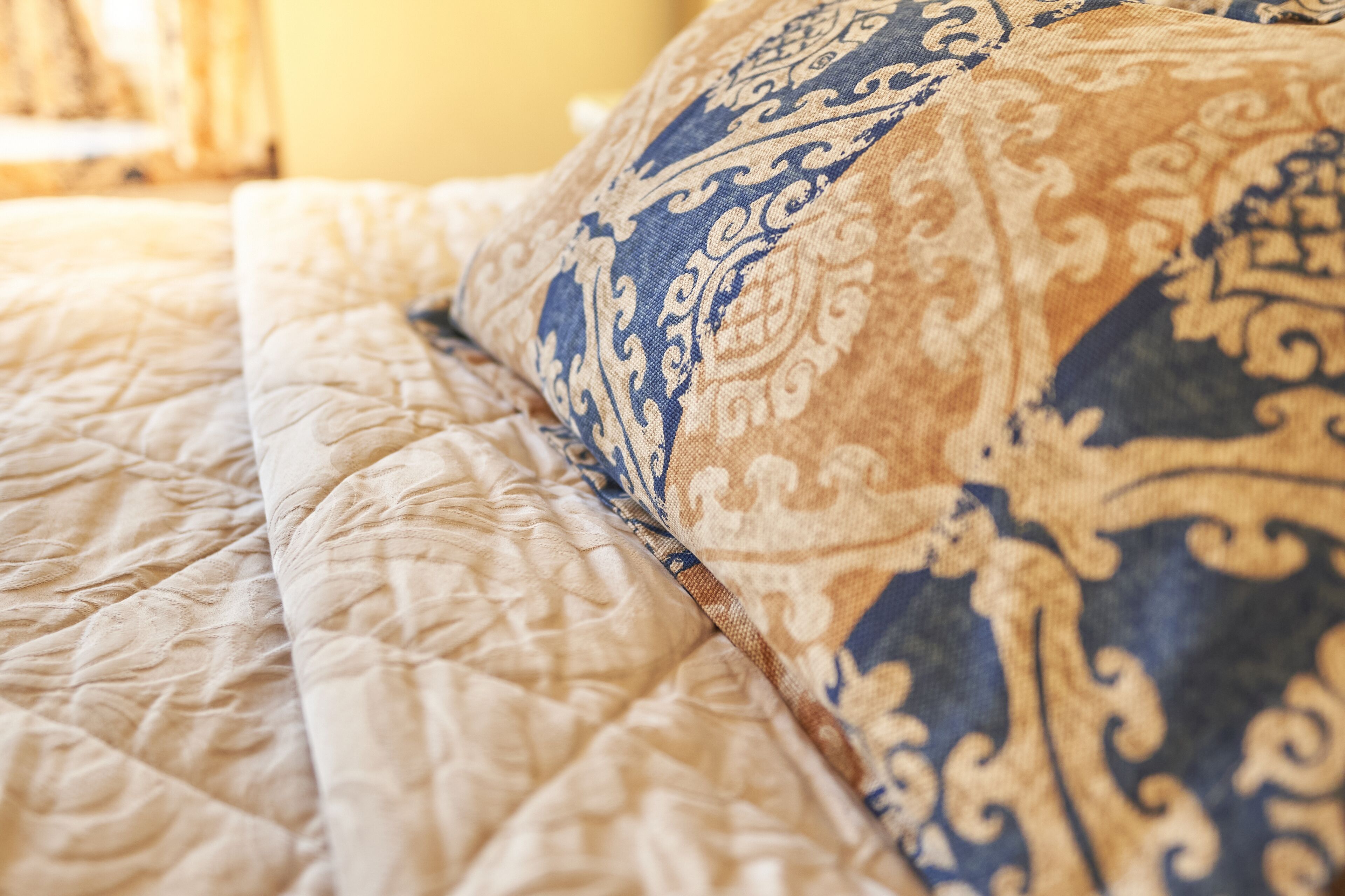 A close-up of a bed with a quilted headboard and a decorative pillow.