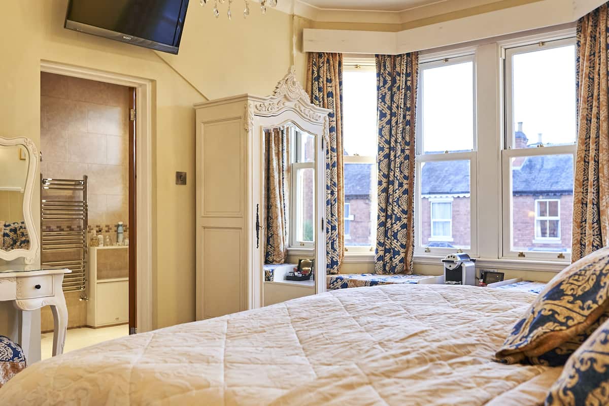 A bedroom with a large bed, a vanity with a mirror, a dresser, and a window with curtains.