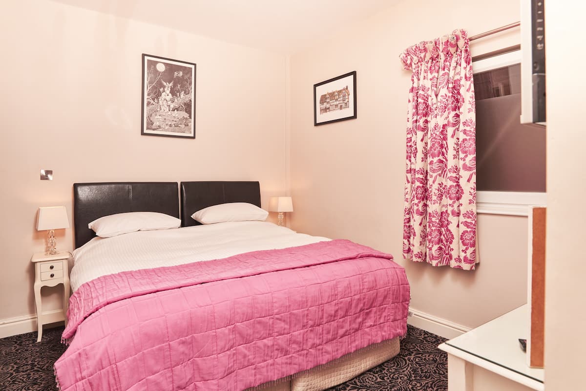 A neatly made bed with a pink quilt, two bedside tables with lamps, and two framed pictures on the wall.