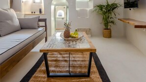 A cozy, well-lit interior with a sofa, a dining table with fruits, a potted plant, and a TV mounted on the wall. - Exi Castle Suites (Santorini)