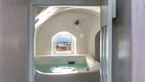 A small, enclosed bathroom with a window providing a view of the outside. - Exi Castle Suites (Santorini)