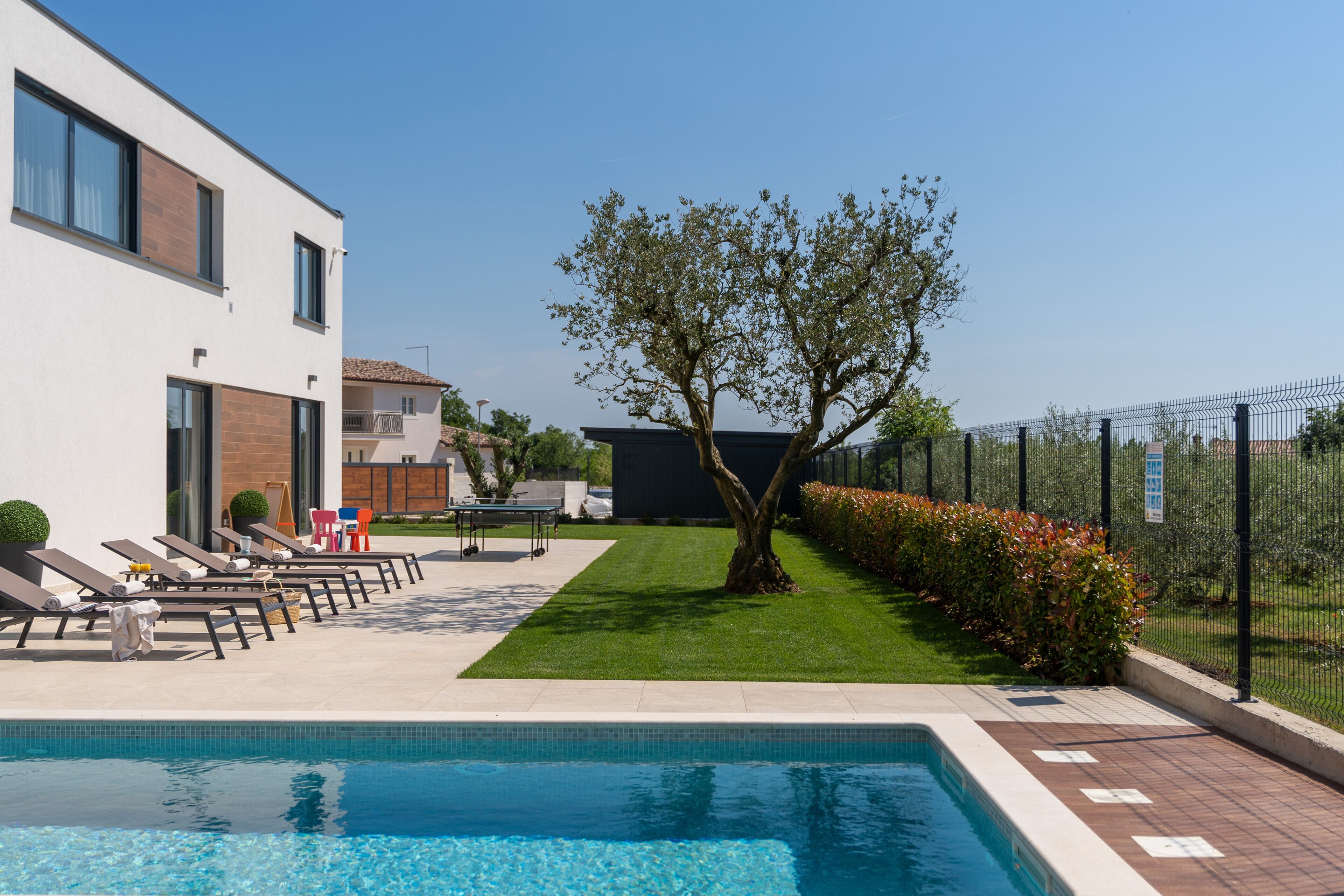 Un espace piscine avec des chaises longues, une petite table et un arbre.