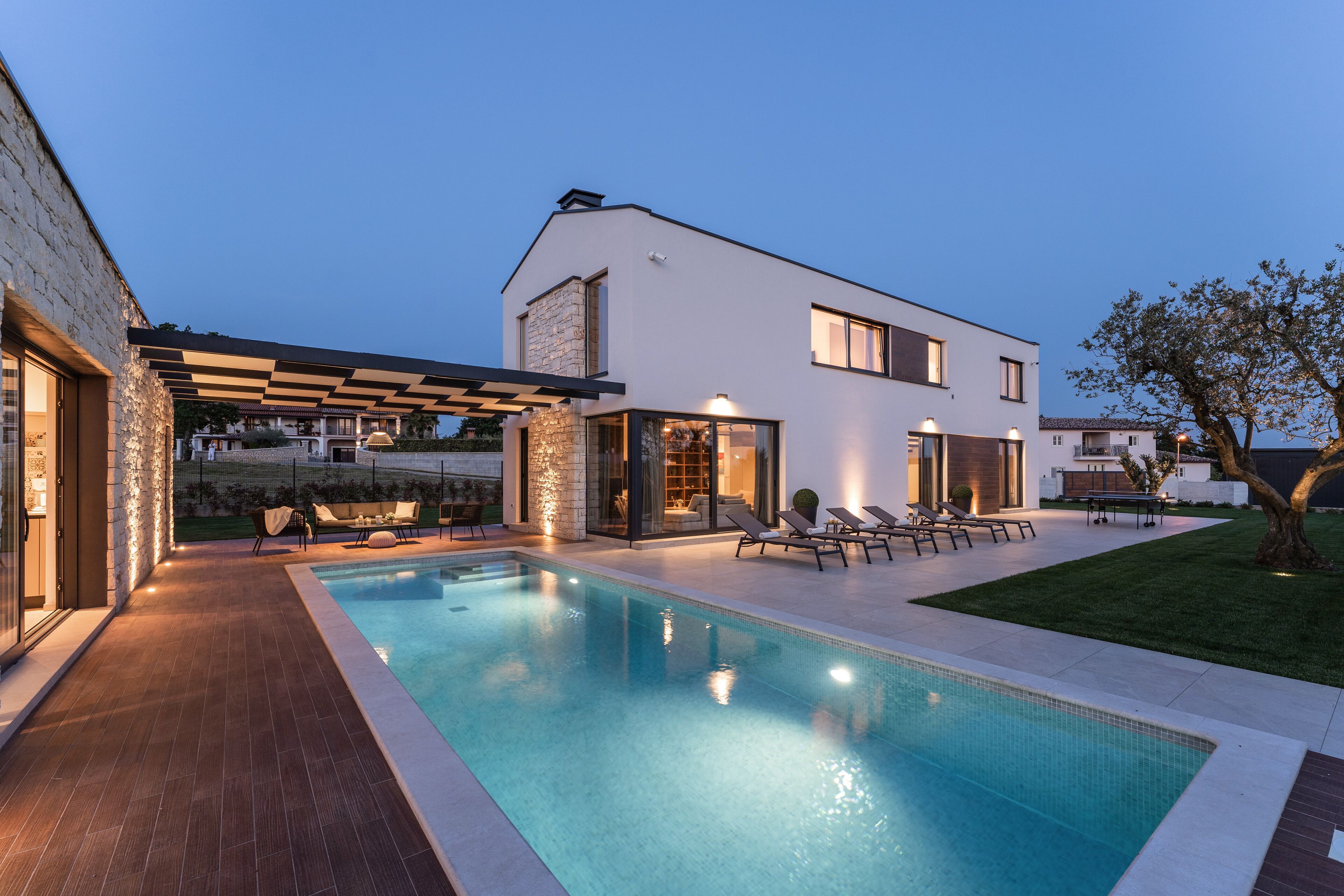 Una casa moderna con piscina, mobiliario exterior y un patio bien iluminado.