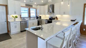 A modern kitchen with white cabinetry, a large island with bar stools, stainless steel appliances, and pendant lighting.