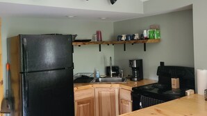 Una cocina compacta con un refrigerador negro, armarios de madera, encimera de madera y estufa negra.