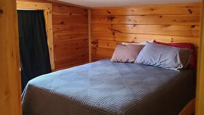 Un dormitorio con paneles de madera, una cama individual, una ventana con cortina negra y suelo de madera.