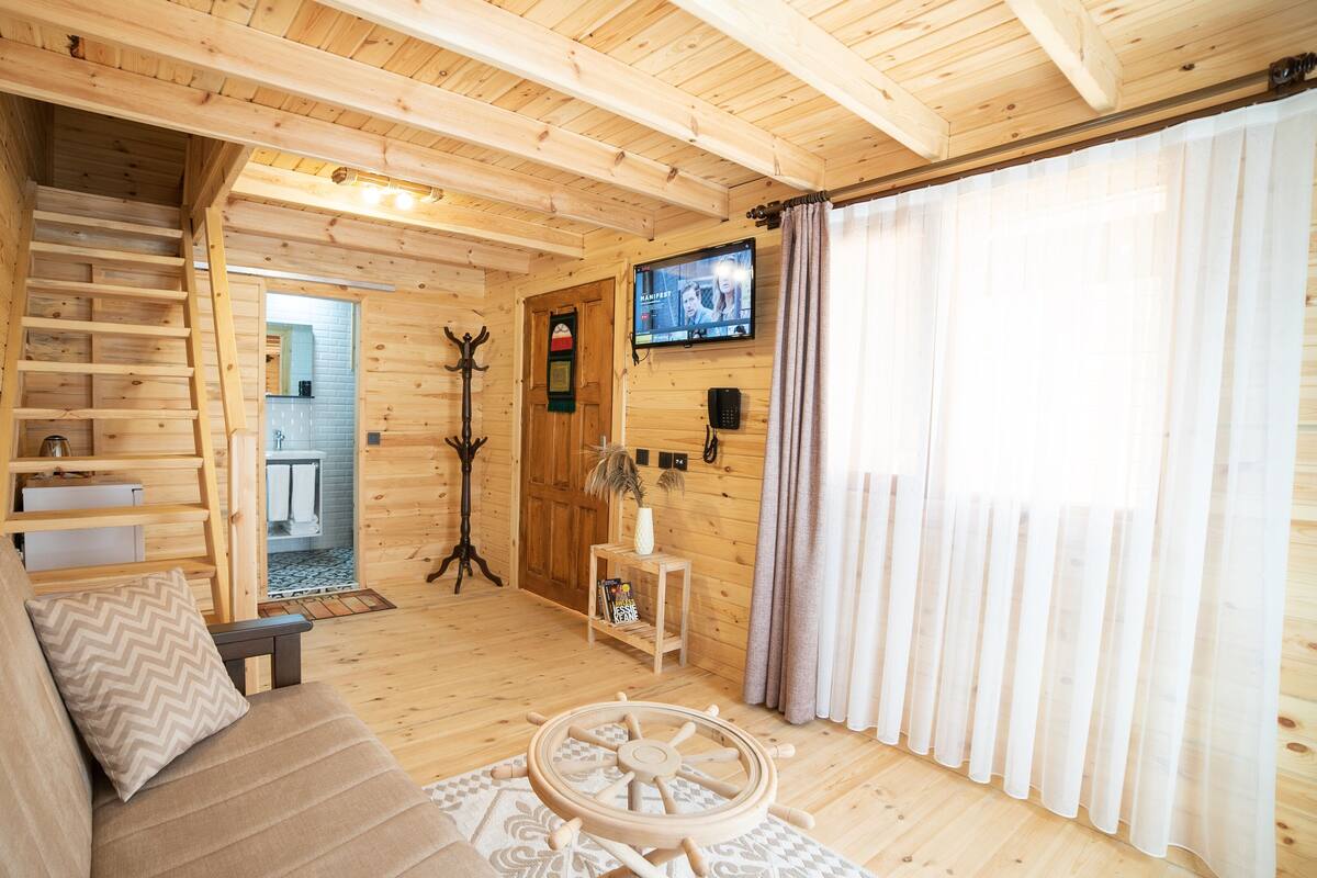 Un interior de madera con un sofá, una mesa pequeña, un televisor y una escalera que sube a un nivel superior.