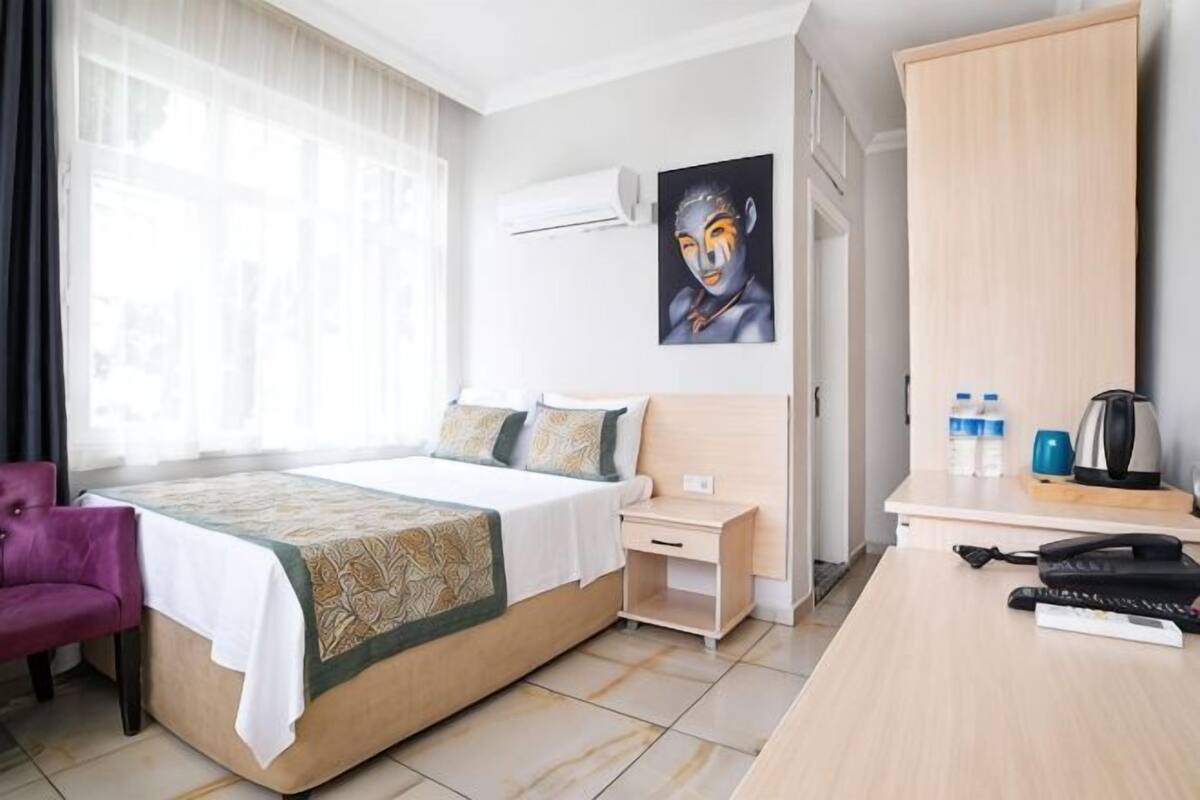 Una habitación de hotel con cama, escritorio, silla, aire acondicionado y un cuadro en la pared.