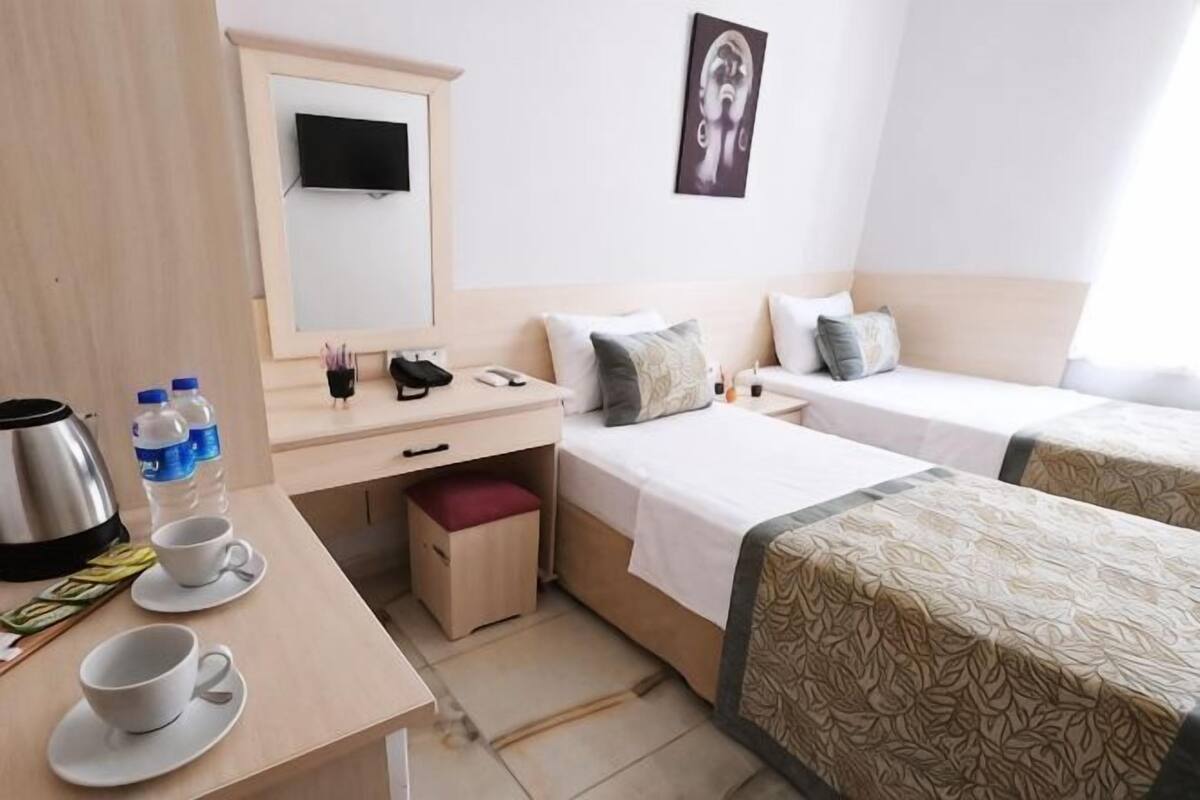 Una habitación de hotel con dos camas individuales, un escritorio con teléfono, cafetera y televisión en la pared.