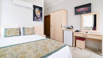 A hotel room with a bed, a desk, a wardrobe, a mirror, a TV, and a small fridge.