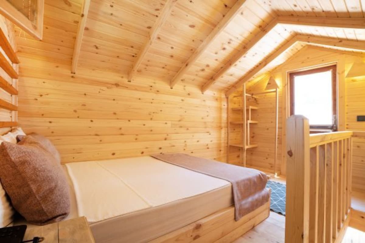 A wooden cabin room with a bed, a window, and a wooden railing.