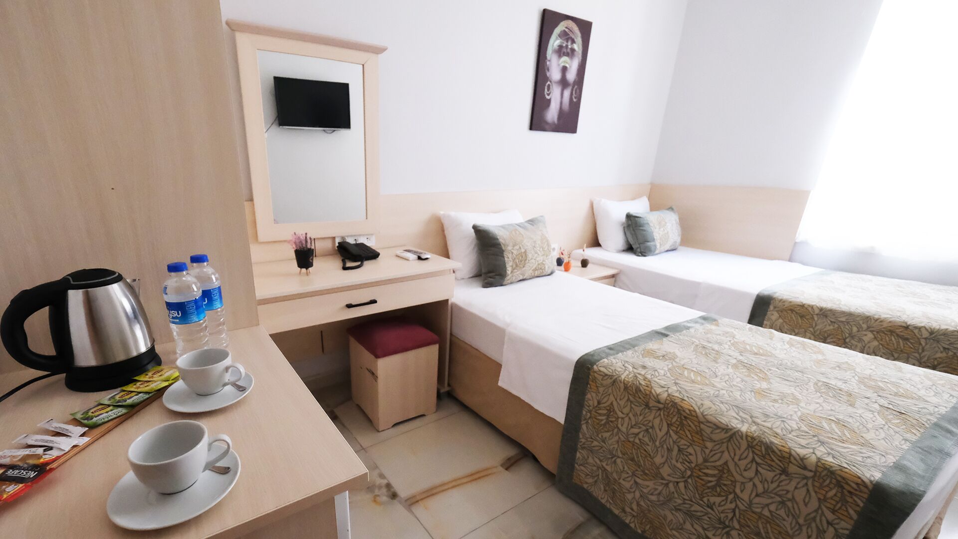 Habitación de hotel con dos camas individuales, un escritorio con hervidor, tazas y una mesita con aperitivos.