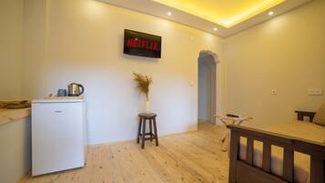 A compact living space with a kitchenette, a small dining area, and a wall-mounted television displaying the Netflix logo.