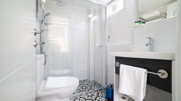 A modern bathroom with a glass-enclosed shower, a white toilet, a black and white patterned floor, and a sink with a towel rack. - My Home Hotel Antalya City Center (Antalya)