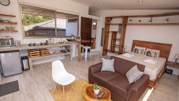 Een ruimtelijk ingerichte leefruimte met kitchenette, een bank, een eethoek en een bed.