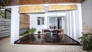 Een modern terras met een houten tafel en stoelen, een kleine potplant en een bamboe zonwering voor een raam.