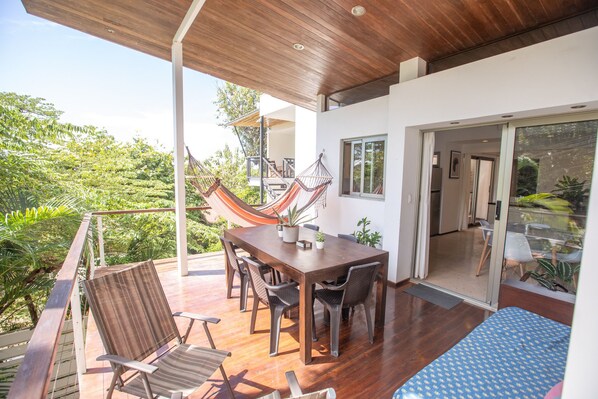 Une terrasse en bois avec une table et des chaises, un hamac et une vue sur la verdure.