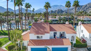 Ein zweistöckiges Haus mit rotem Ziegeldach, einer blauen Garagentür und einem Pool im Hintergrund.