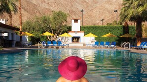Ein Poolbereich mit Liegestühlen und Sonnenschirmen, ein Gebäude mit Kamin und Berge im Hintergrund.