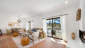 Ein großzügiger Wohnbereich mit einer Couch, einem Couchtisch und Sesseln, einem Esstisch und einem Balkon mit Blick auf Palmen und Berge.