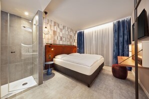 A modern hotel room with a glass-enclosed shower, a wooden headboard, a large bed, a small round table, and a TV mounted on the wall. - H2 Hotel Mainz (Mainz)