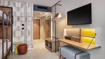 A modern hotel room with a wooden bench, a small table, a mirror, and a TV mounted on the wall.