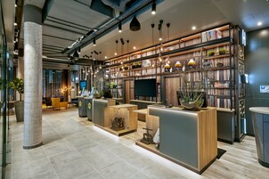Un moderno vestíbulo de hotel con mostrador de recepción, zona de estar y una estantería llena de libros y objetos decorativos.