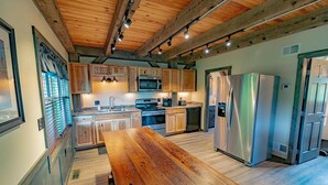 A modern kitchen with wooden cabinets, stainless steel appliances, and a wooden dining table. - Panoramic Point Cabin - Beautiful Mountain Retreat for Families (Ohiopyle)