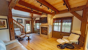 A spacious living room with a stone fireplace, wooden beams, and leather sofas. - Panoramic Point Cabin - Beautiful Mountain Retreat for Families (Ohiopyle)