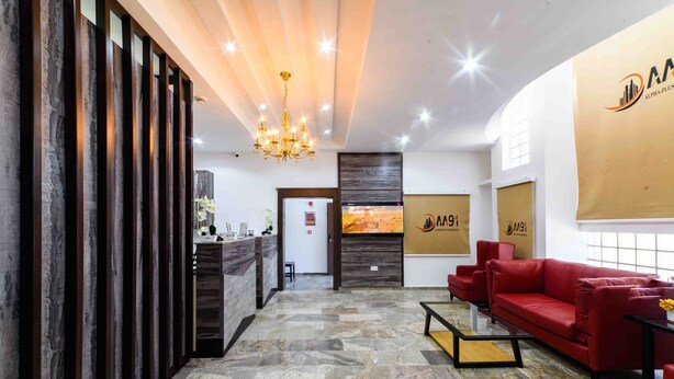A reception area with a stone floor, a red sofa, a chandelier, and a reception desk. - Alpha-Plus Apartments 91 Utako (Abuja)