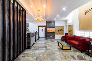 A reception area with a stone floor, a red sofa, a chandelier, and a reception desk. - Alpha-Plus Apartments 91 Utako (Abuja)