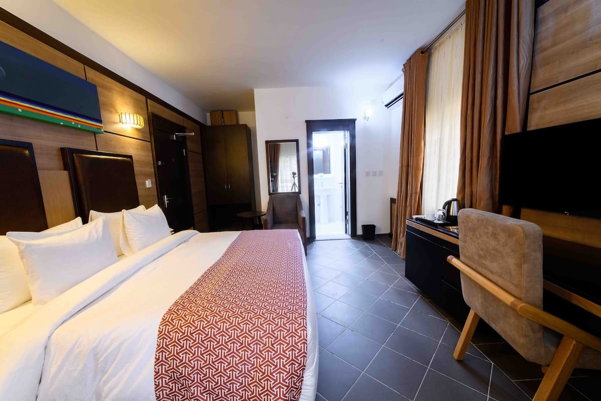 A hotel room with a large bed, a flat-screen TV, a desk with a chair, and a wardrobe.