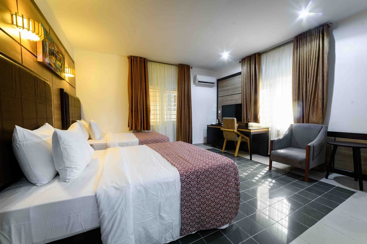 A hotel room with two beds, a desk, a chair, and an air conditioning unit.