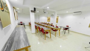 A conference room with a long table and red chairs, white walls, and a projector. - Alpha-Plus Apartments 91 Utako (Abuja)