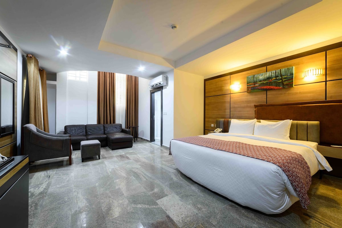 A hotel room with a large bed, a sofa, a desk, and a painting on the wall.