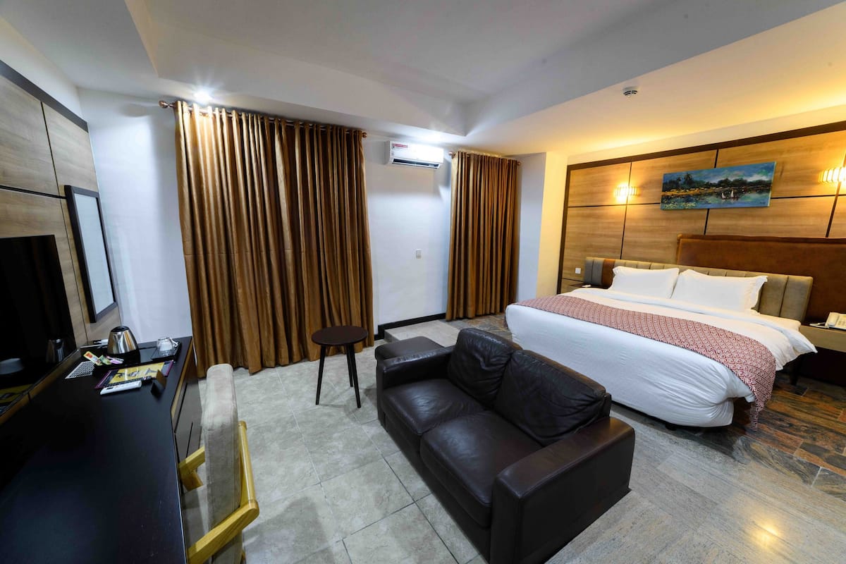A hotel room with a bed, a leather sofa, a desk with a chair, and a television.