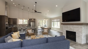 A modern living room with a fireplace, a large TV, and a dining area with natural light. - Home Across from Purg - Hot Tub, Ping Pong, Foosball, AC, Multiple Decks (Durango)