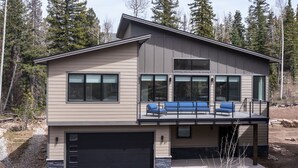 A two-story house with a garage, a balcony with blue chairs, and a stone foundation. - Home Across from Purg - Hot Tub, Ping Pong, Foosball, AC, Multiple Decks (Durango)