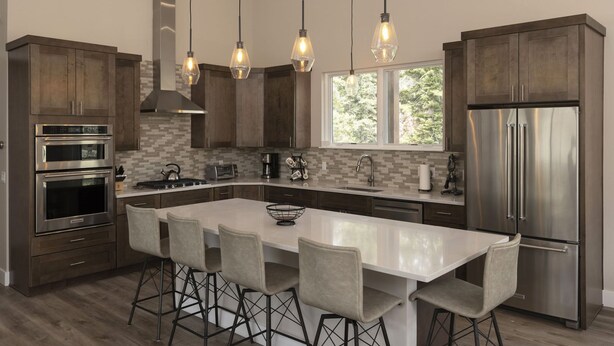 A modern kitchen with dark wood cabinets, stainless steel appliances, a large island with bar stools, and pendant lighting. - Home Across from Purg - Hot Tub, Ping Pong, Foosball, AC, Multiple Decks (Durango)