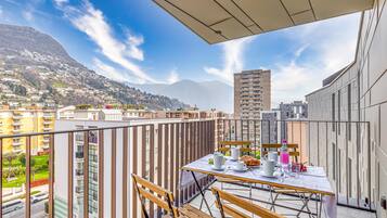 A balcony with a table set for two, overlooking a cityscape with mountains in the distance.