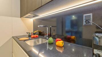 A modern kitchen with a stainless steel sink, a built-in range hood, and a countertop with a cutting board, tomatoes, and bell peppers.