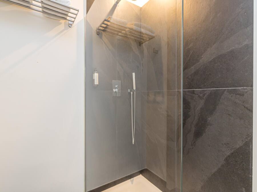 Une salle de bain moderne avec une douche à l’italienne en verre, un porte-serviettes et un mur en marbre.