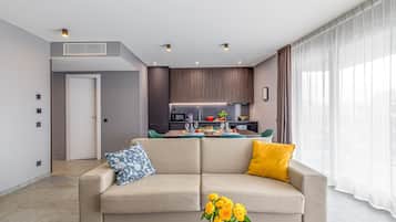 A modern living room with a sofa, a coffee table with flowers, and a kitchen in the background.