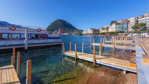 A waterfront dock with a boat, clear water, and a mountain in the background. - ICON H Lugano – Luxury Suites & Apartments (Lugano)